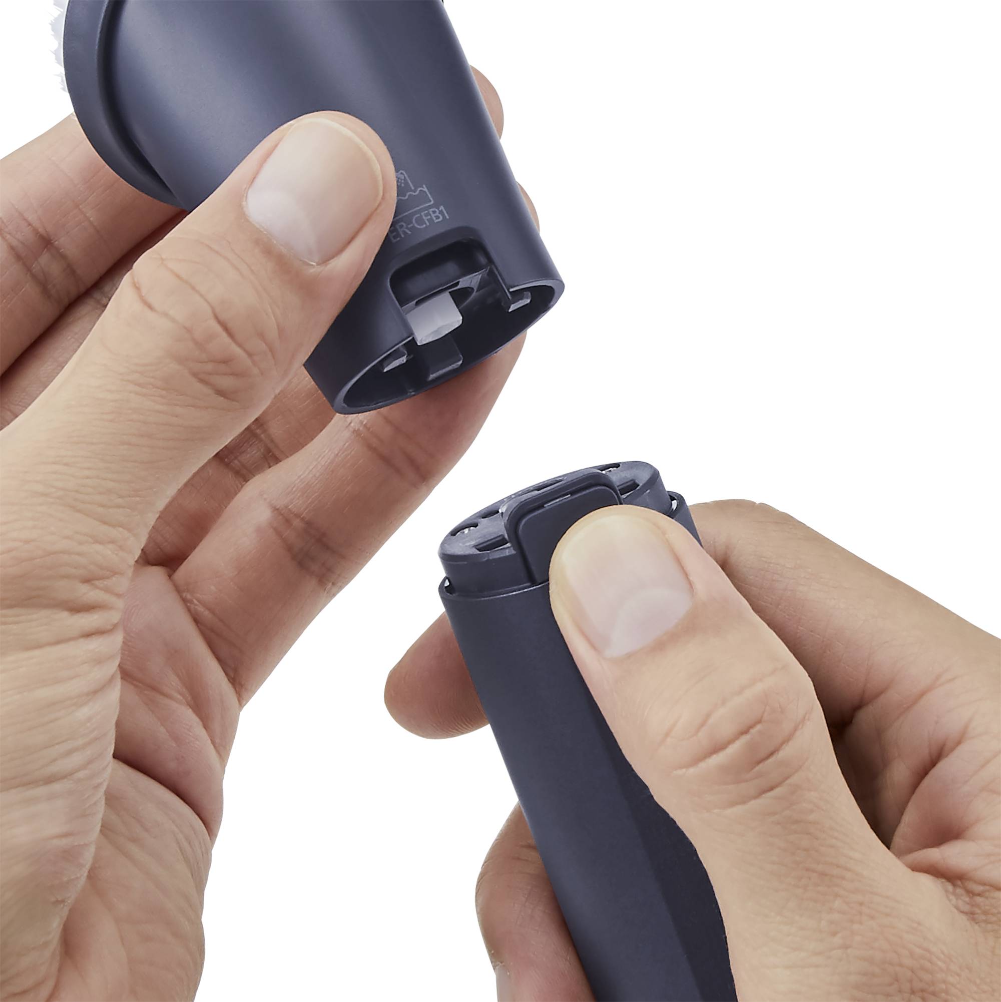 Two hands are opening an electric razor attachment. One hand is holding the lower part, while the other is removing the upper casing.