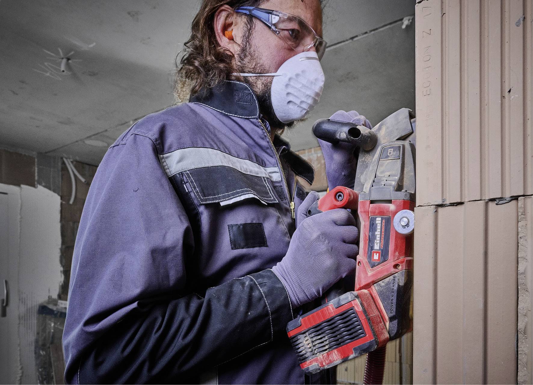 A person is working with power tools on a wall. Wearing safety glasses, a mask and gloves. Renovation or construction work.