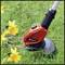 A red lawn trimmer is cutting grass next to yellow daffodils.