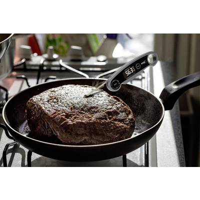 A large piece of meat in a pan is being measured with a digital thermometer showing 56.3°C.