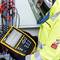 A technician in protective clothing is using an electronic measuring device on a cabling installation to analyse data.