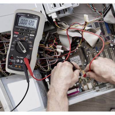 A person is measuring the current flow on an open computer circuit board with a multimetre. Many cables are visible.