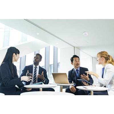Four individuals in business attire are seated at a table in a modern office, engaging in an intense discussion while using a laptop and notebooks.