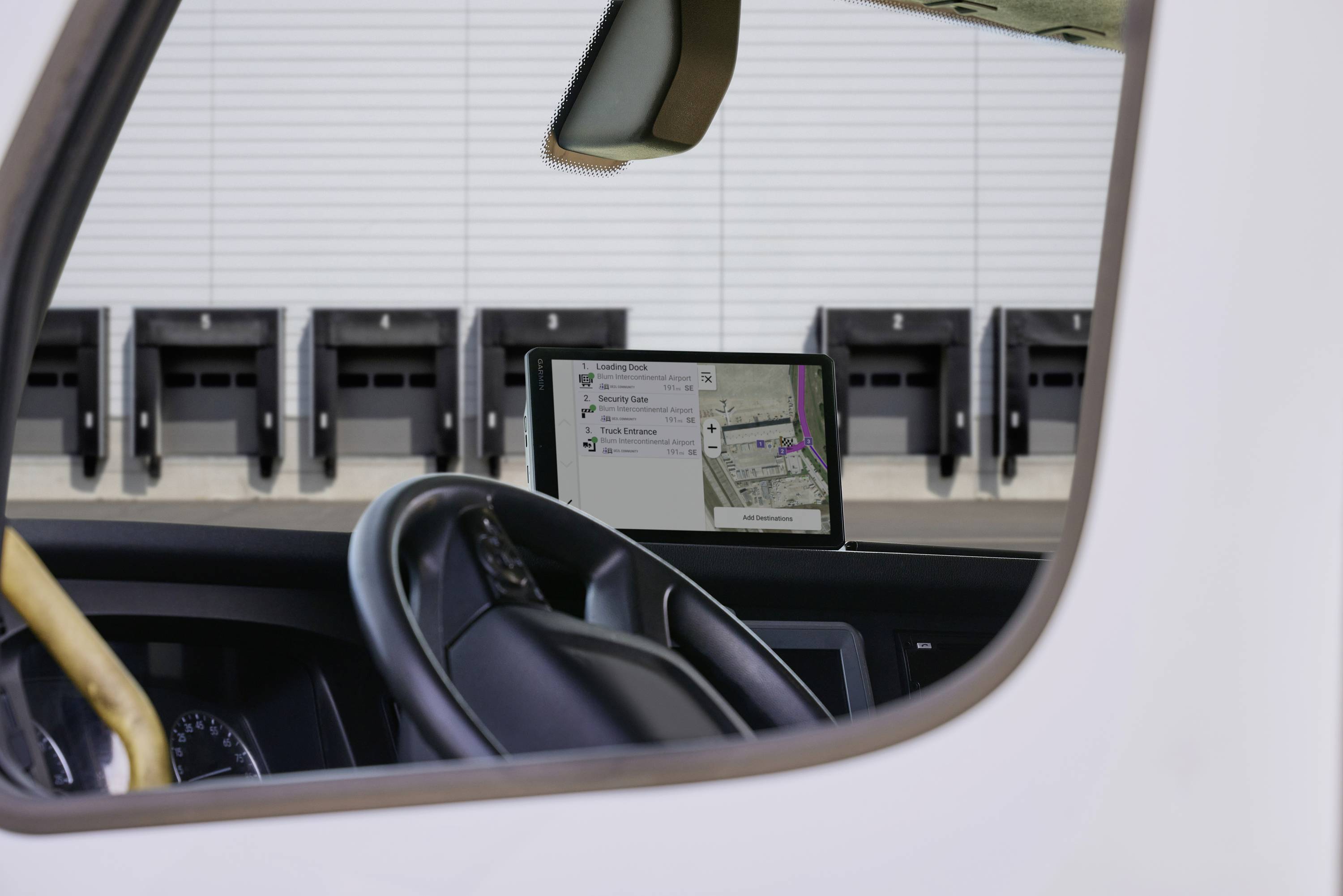 Interior view of a vehicle showing the steering wheel and a screen with a navigation map. Background: Loading ramps of a building.