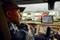 A lorry driver sits in his vehicle on a car park full of trucks. A satellite navigation system shows a route.