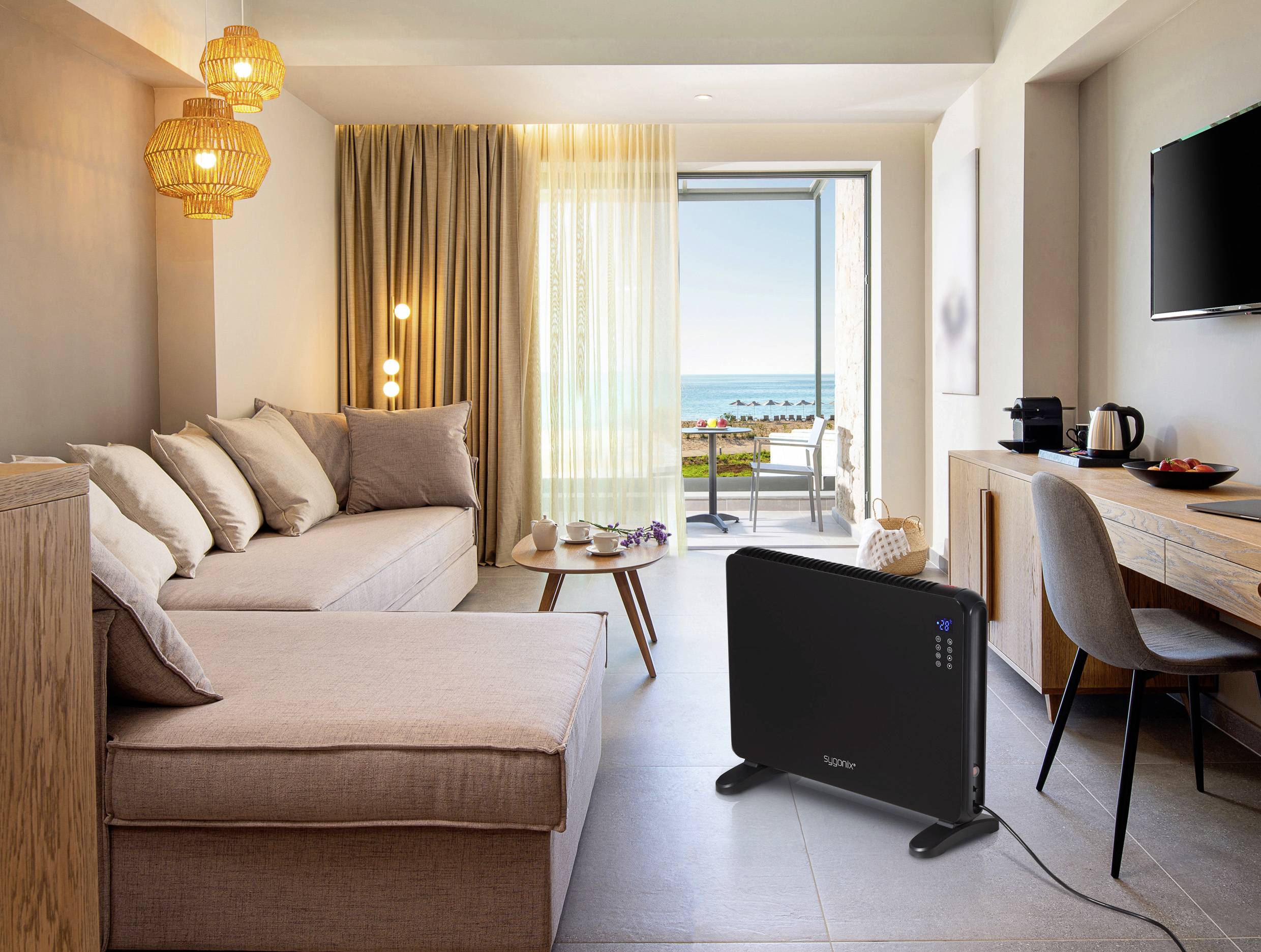 A modern living room with a sofa, coffee table and large window overlooking the sea. A heater is standing on the floor.