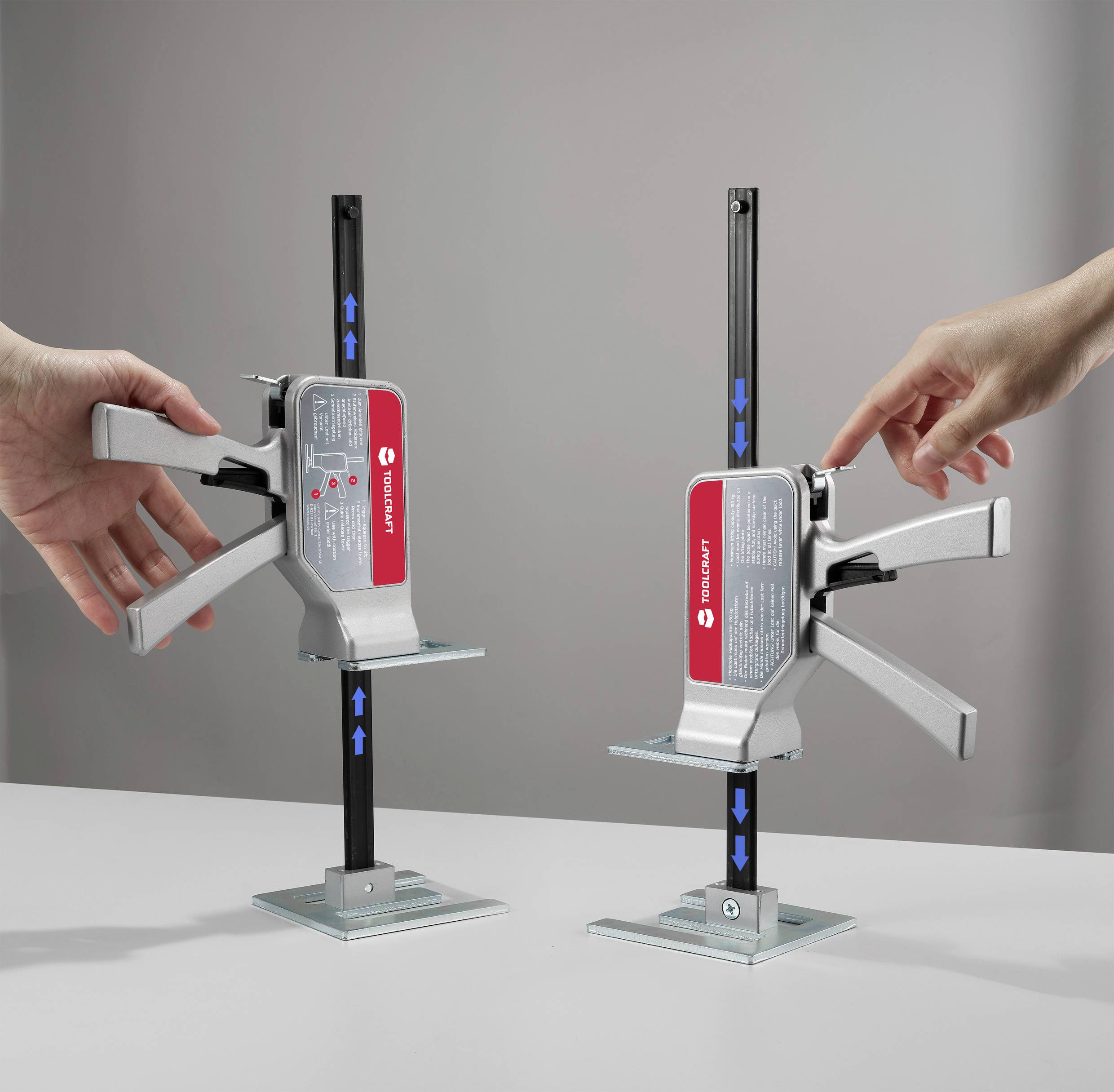 Two hands operate levers on two fixing clamps with a metal rod and red label on a grey table in a neutral space.