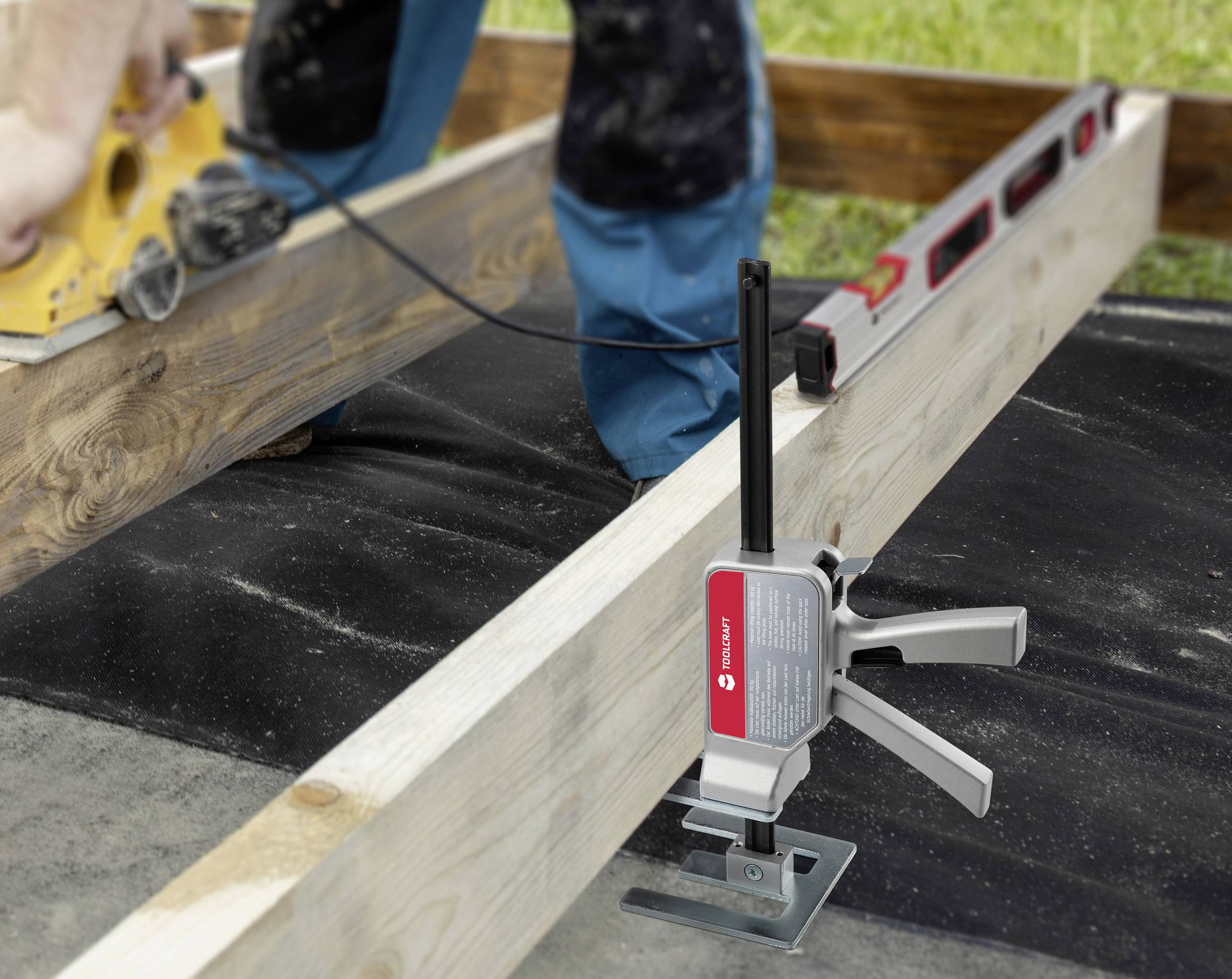 A person is using an electric tool to sand wood. Another tool is holding two beams together. A spirit level is resting on the wood.