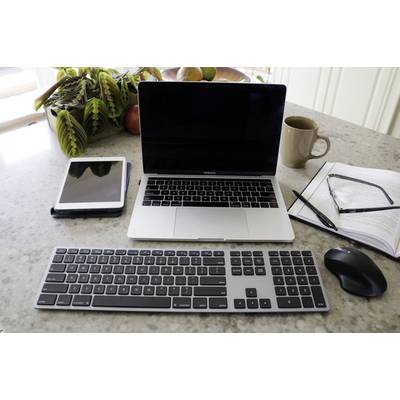 On a desk sit a laptop, a tablet, an external keyboard, a mouse, a mug, and an open notebook.