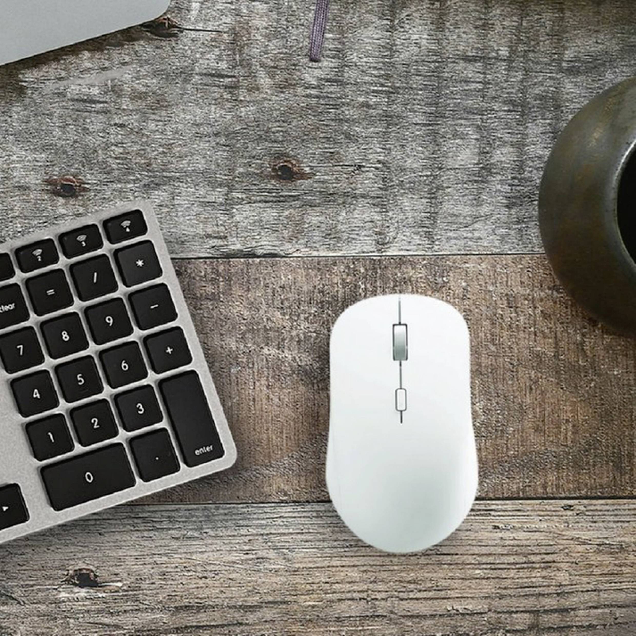 A white computer mouse is lying on a wooden table next to a black keyboard and a dark mug.
