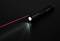 A black torch on a dark surface emits a red laser beam. The light cone is slightly visible.