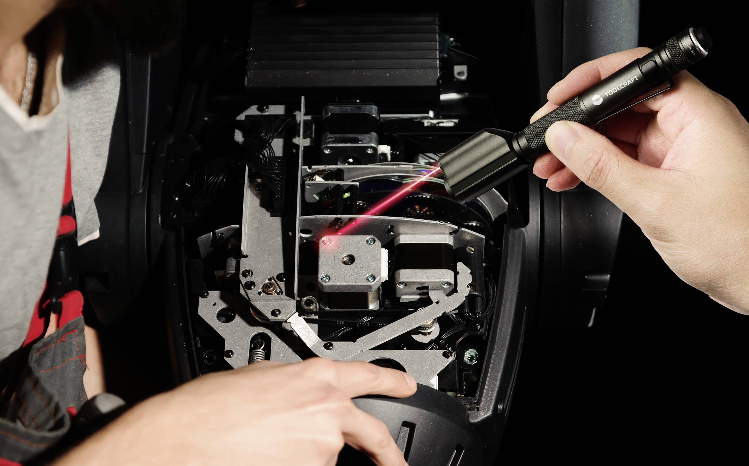 A person is pointing a laser light at technical components inside an opened device, possibly for diagnostic or repair purposes.