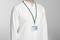 A person is wearing a white shirt and an ID card on a green lanyard around their neck. The ID shows a photo and text, but is illegible.