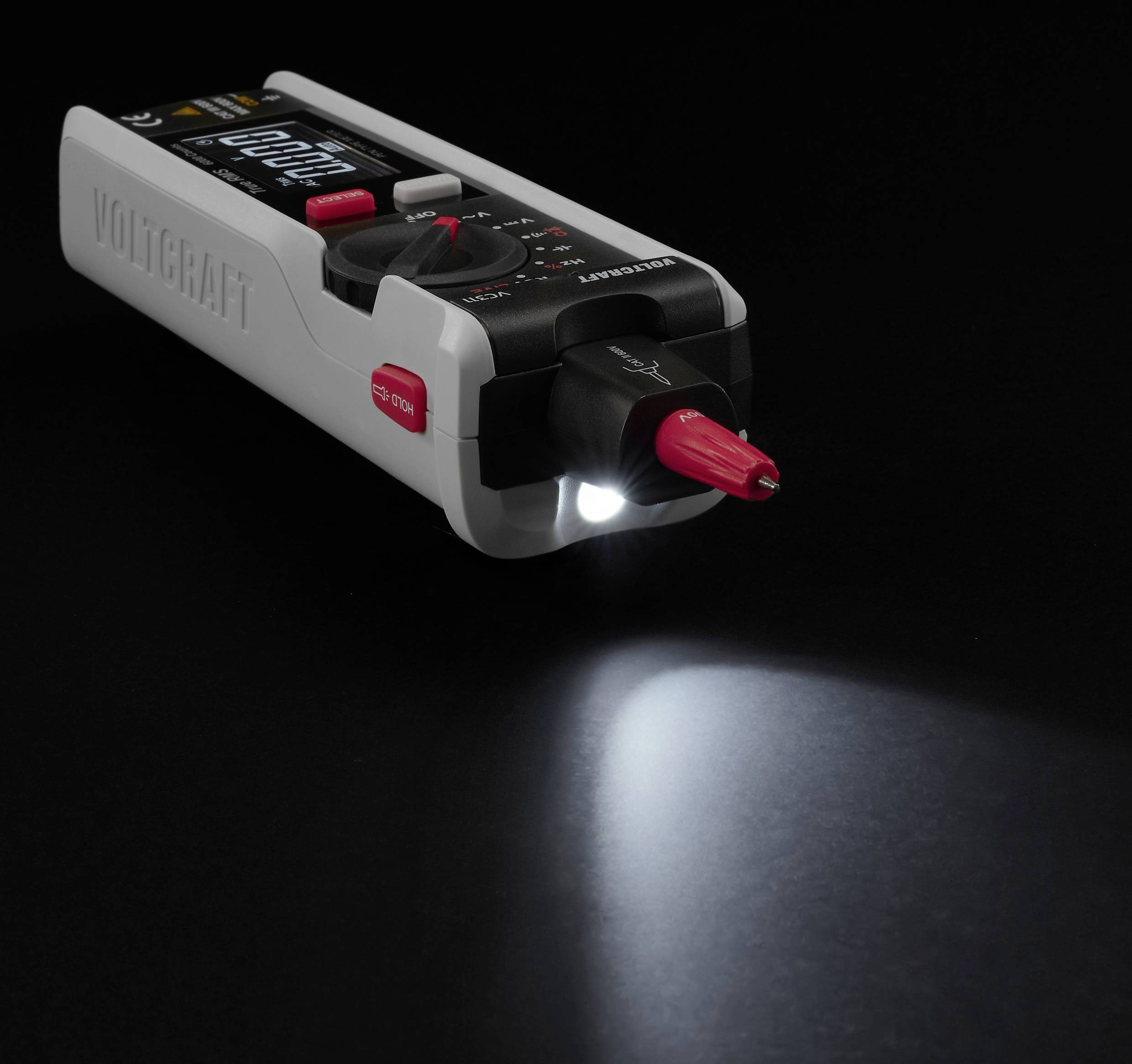 A digital multimeter rests on a black surface, featuring a lit LED flashlight and visible display.
