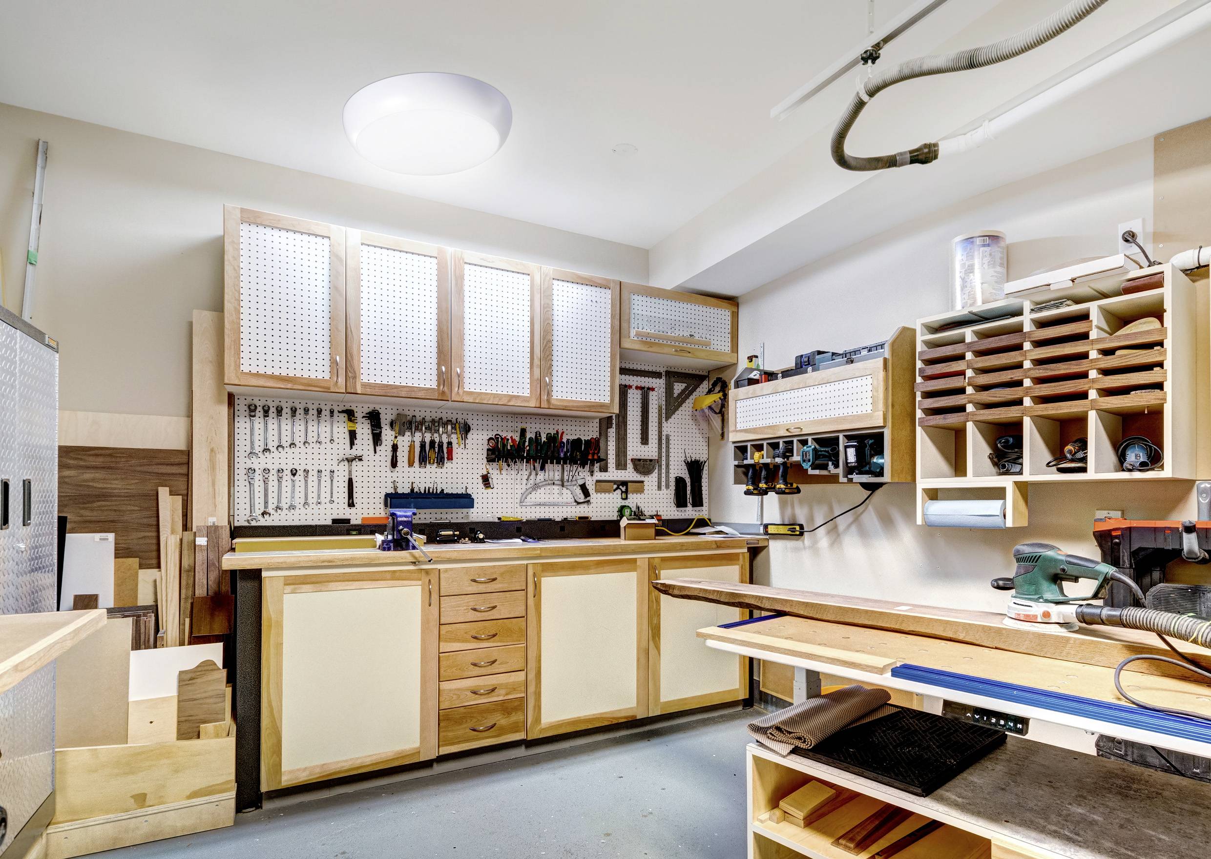 A well-organized workshop featuring tools hanging on a pegboard, wooden workbenches, and shelves with woodworking supplies.