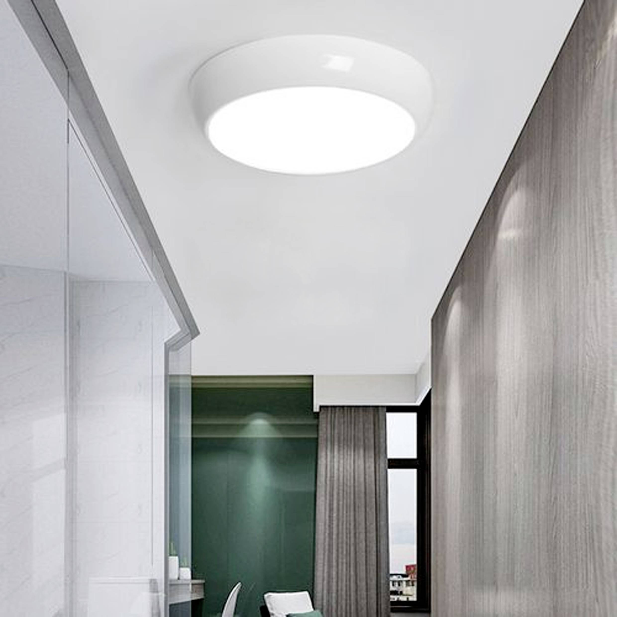 Ceiling-mounted circular LED light illuminating a modern room with large windows and minimalistic decor.