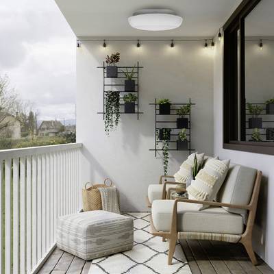 A cozy balcony with string lights, chairs, and a pouf; wall-mounted plants add greenery. A lush landscape is visible in the background.