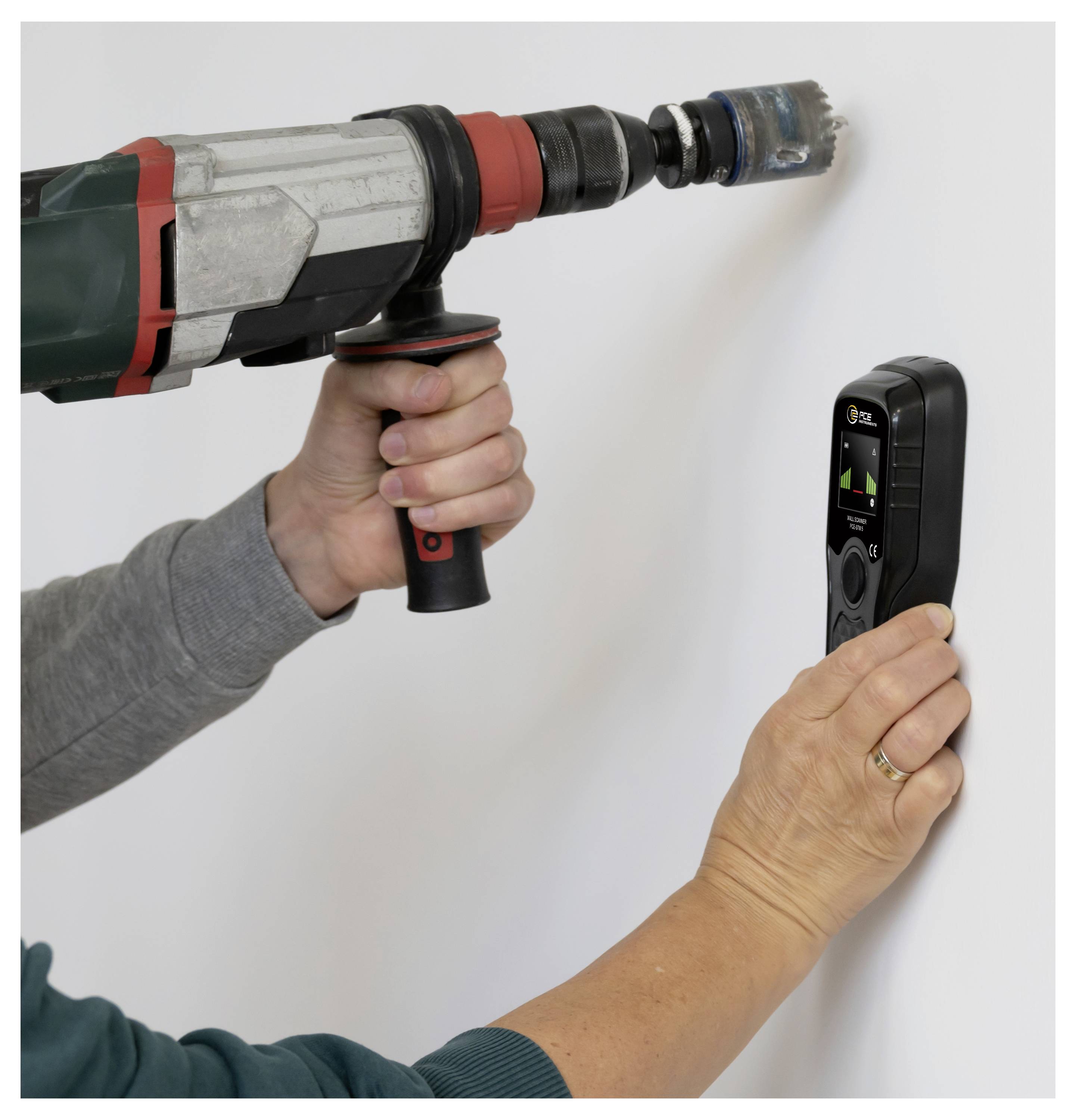 Person using a drill and a handheld detector on a wall to locate hidden studs or wiring.