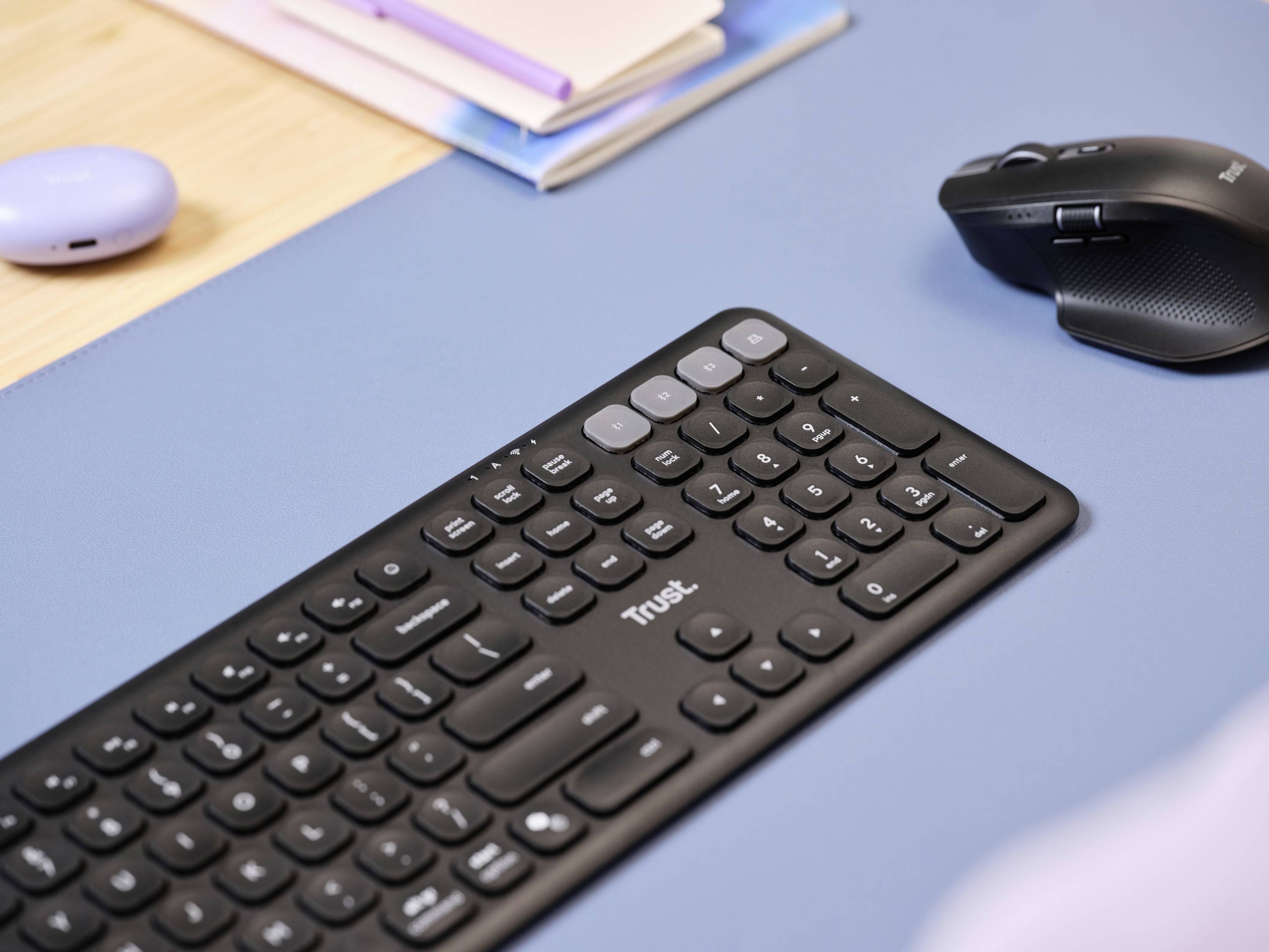 A black keyboard and mouse on a blue desk next to notebooks; office workspace environment.