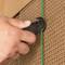 'Close-up of a hand cutting a green plastic string on brown corrugated cardboard with a craft knife.'
