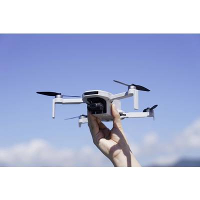 A hand holds a small drone against a blue sky. The drone has four propellers and a camera.