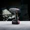 A cordless drill driver on a table with a blurred background. It is grey with a distinctive red switch.