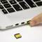A hand is inserting a USB stick into a laptop. An SD card adapter is lying beside it.