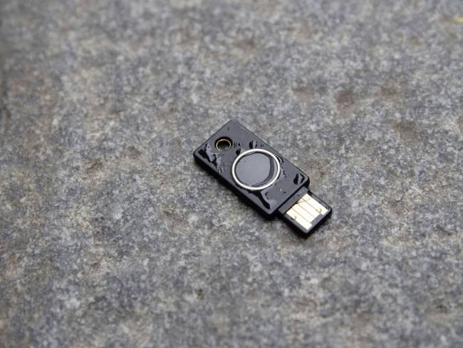 A black USB security key device lies on a grey, stony surface.