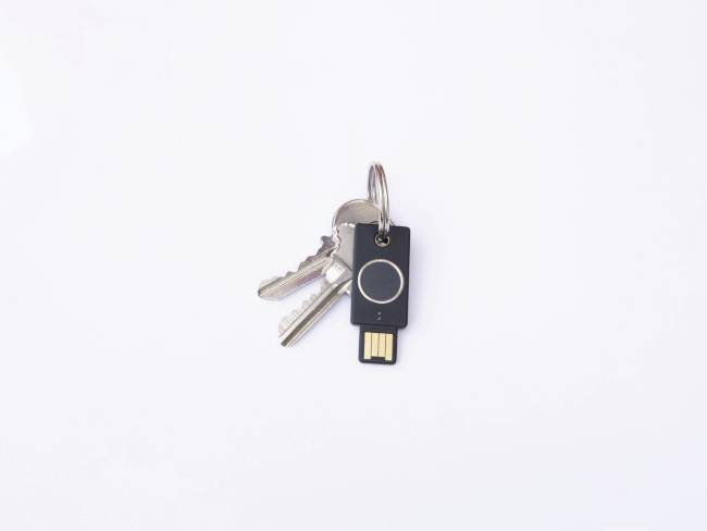 A bunch of keys with two metal keys and a black USB security stick is lying on a white surface.