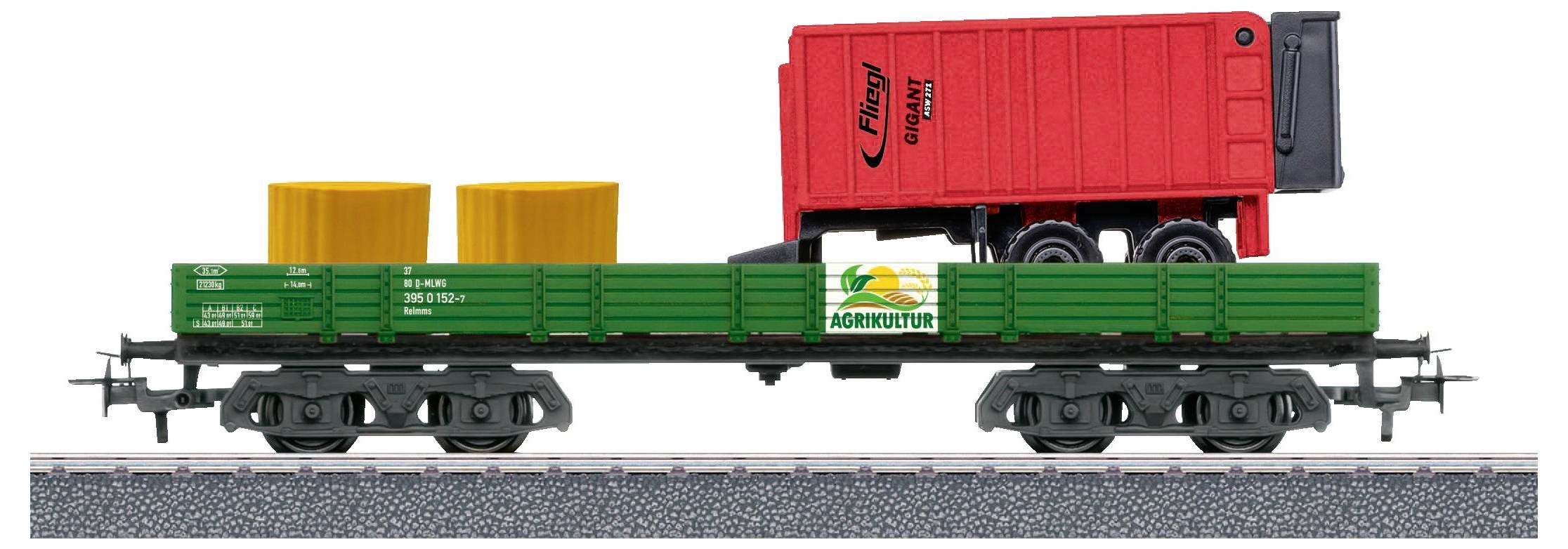 A model train with a green goods wagon is carrying two yellow cylinders and a red container. The container is designed as a trailer.