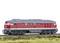 Red model of a diesel locomotive on a railway track with a green-brown meadow landscape in the foreground.