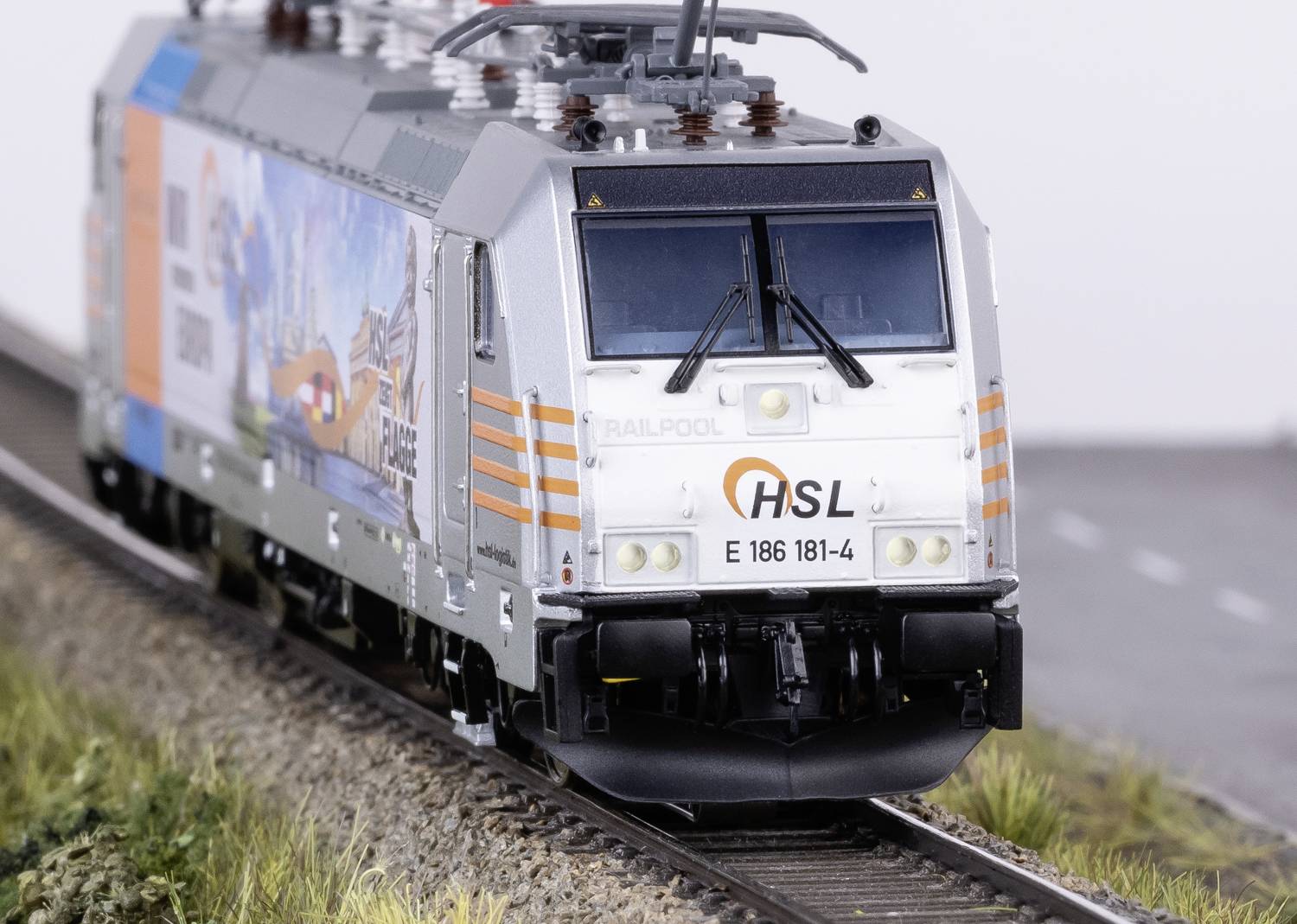 A silver model train with the inscription 'HSL' is travelling on a track, surrounded by grass.