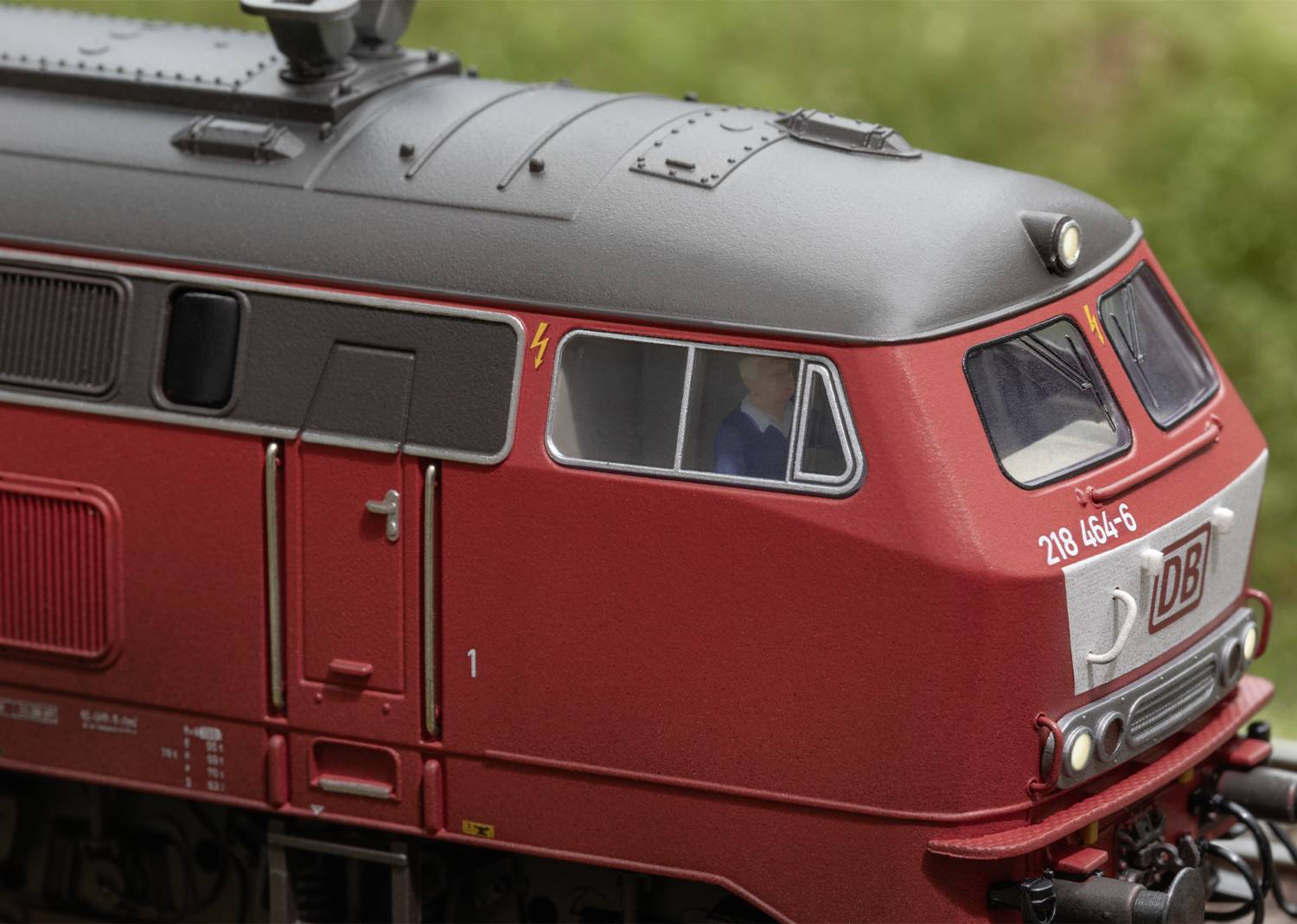 Red model locomotive of Deutsche Bahn with 'DB' inscription on a green background. Details of the locomotive front and side windows are visible.