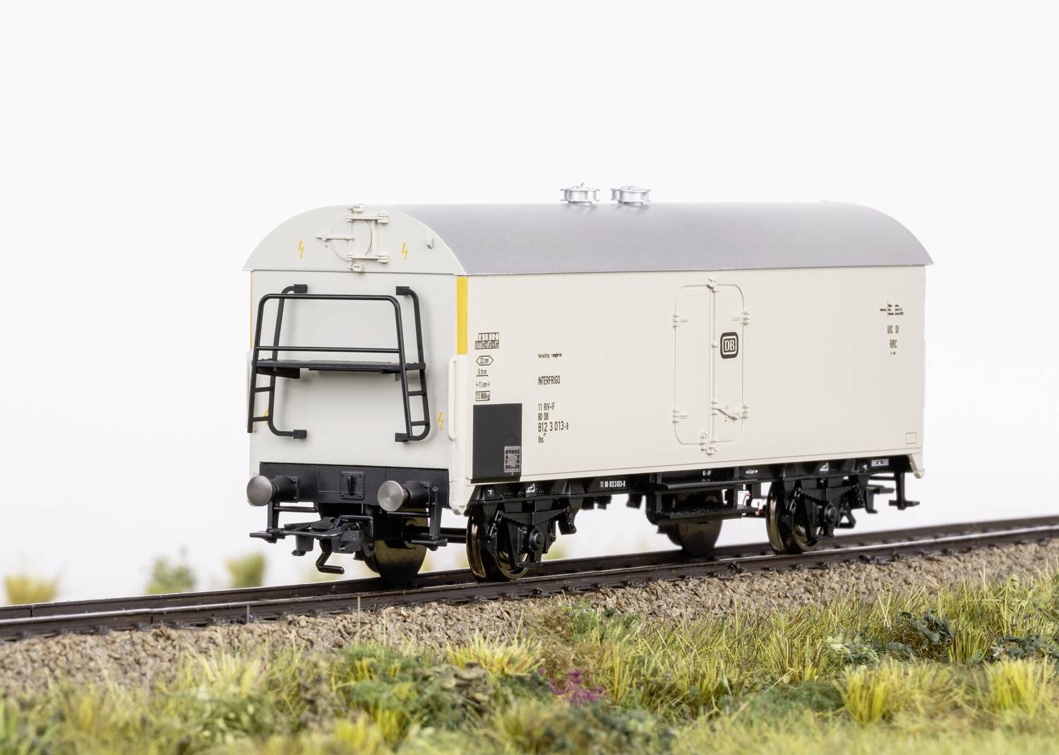 A white goods wagon on a railway track in a rural landscape. The goods wagon has a vehicle identification number and technical markings.