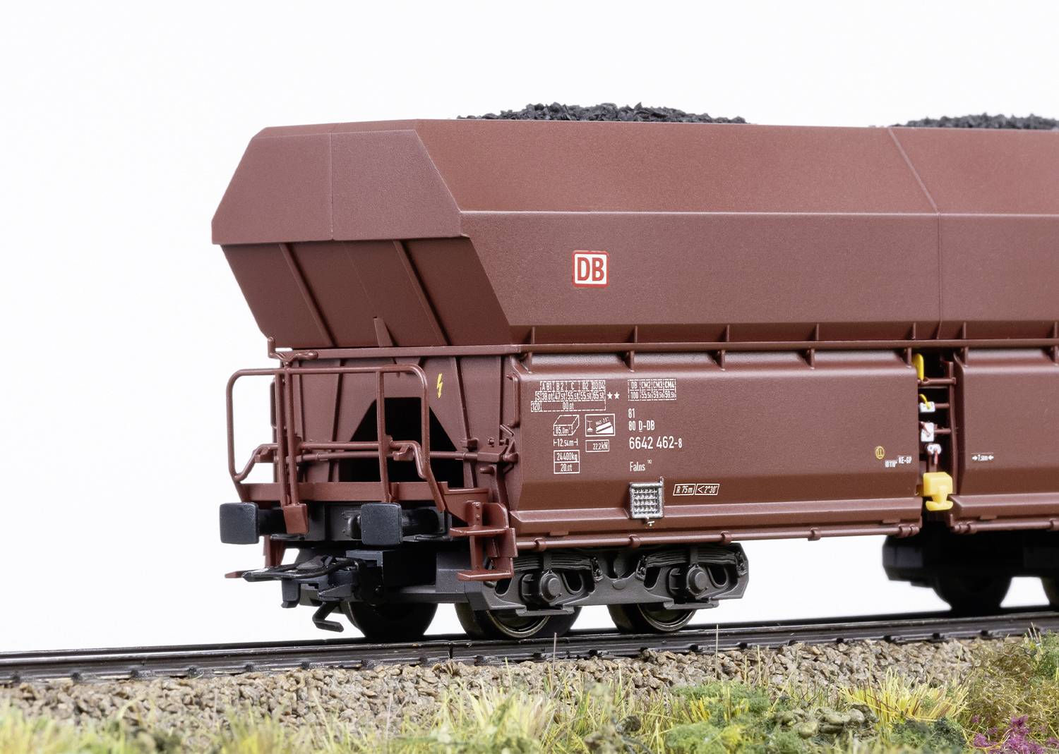 A brown Deutsche Bahn freight wagon is travelling on a railway track, loaded with black coal.