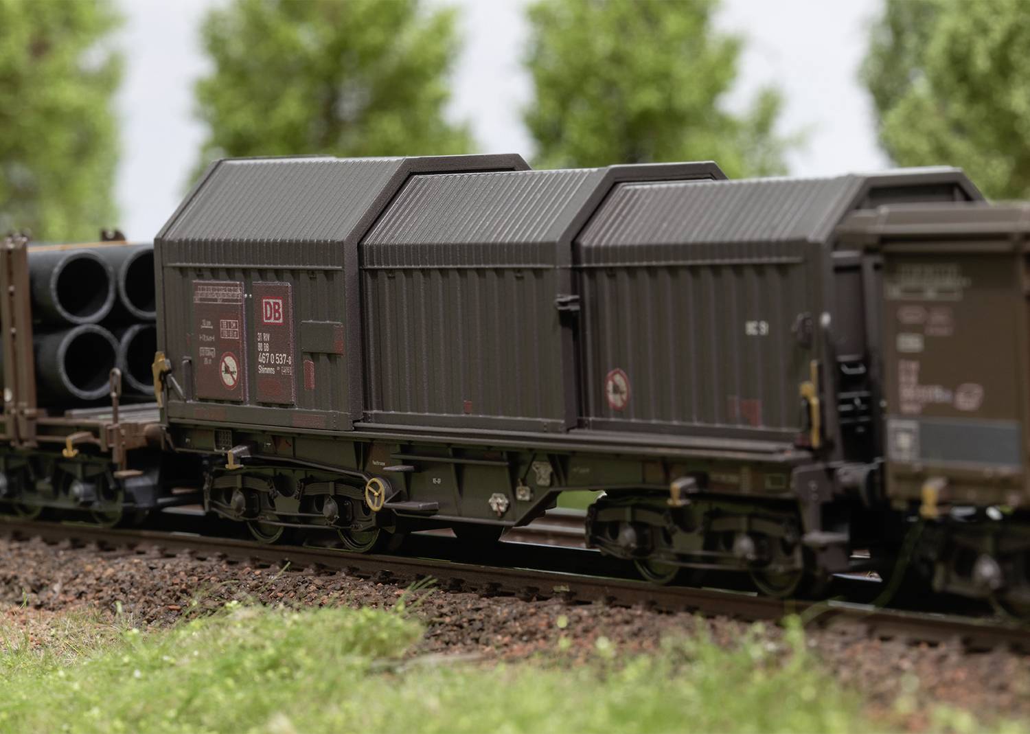 Freight train wagon with brown paintwork travels on railway tracks, surrounded by trees in the background. Transportation of heavy goods.