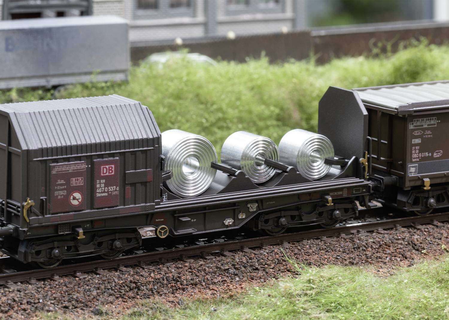 Railway Model: Two freight wagons, one transporting rolled metallic bands. Scenic landscape in the background.