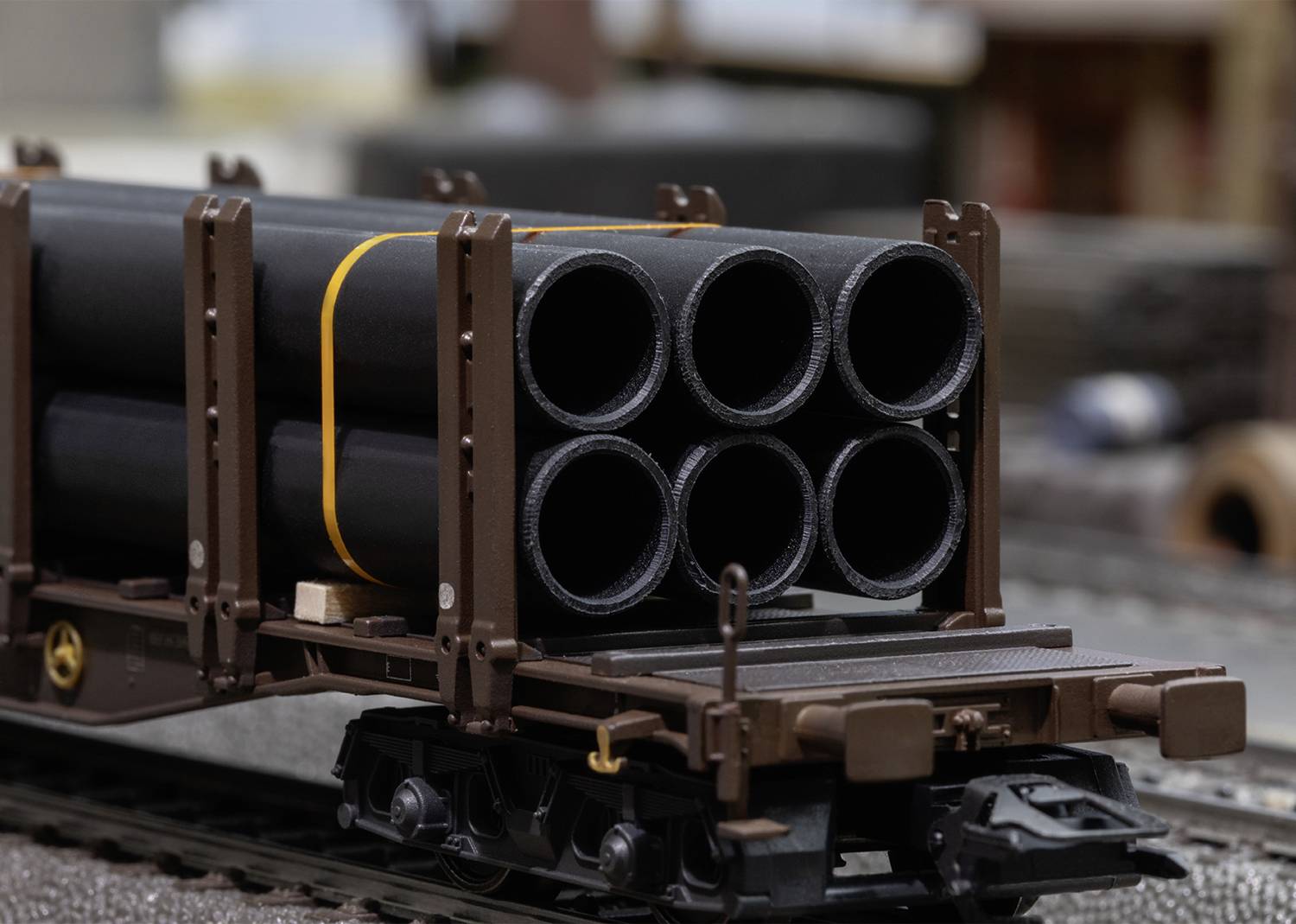 A railway wagon is transporting several black pipes in an industrial area. The pipes are stacked and secured with straps.