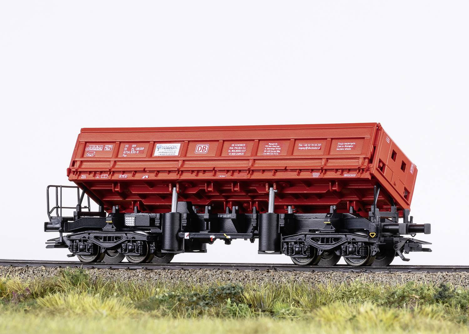 A red model goods wagon is standing on a railway track. The wagon has black wheels and chassis. Text and logos are printed on the surface.