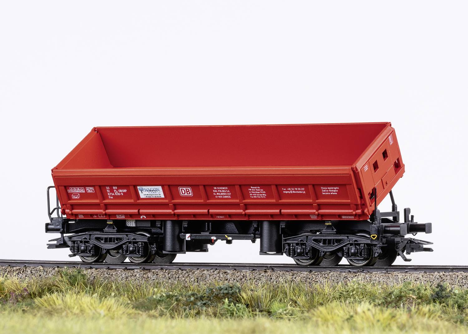 A red railway goods wagon on tracks in a model landscape. The wagon is intricately designed and realistically presented.