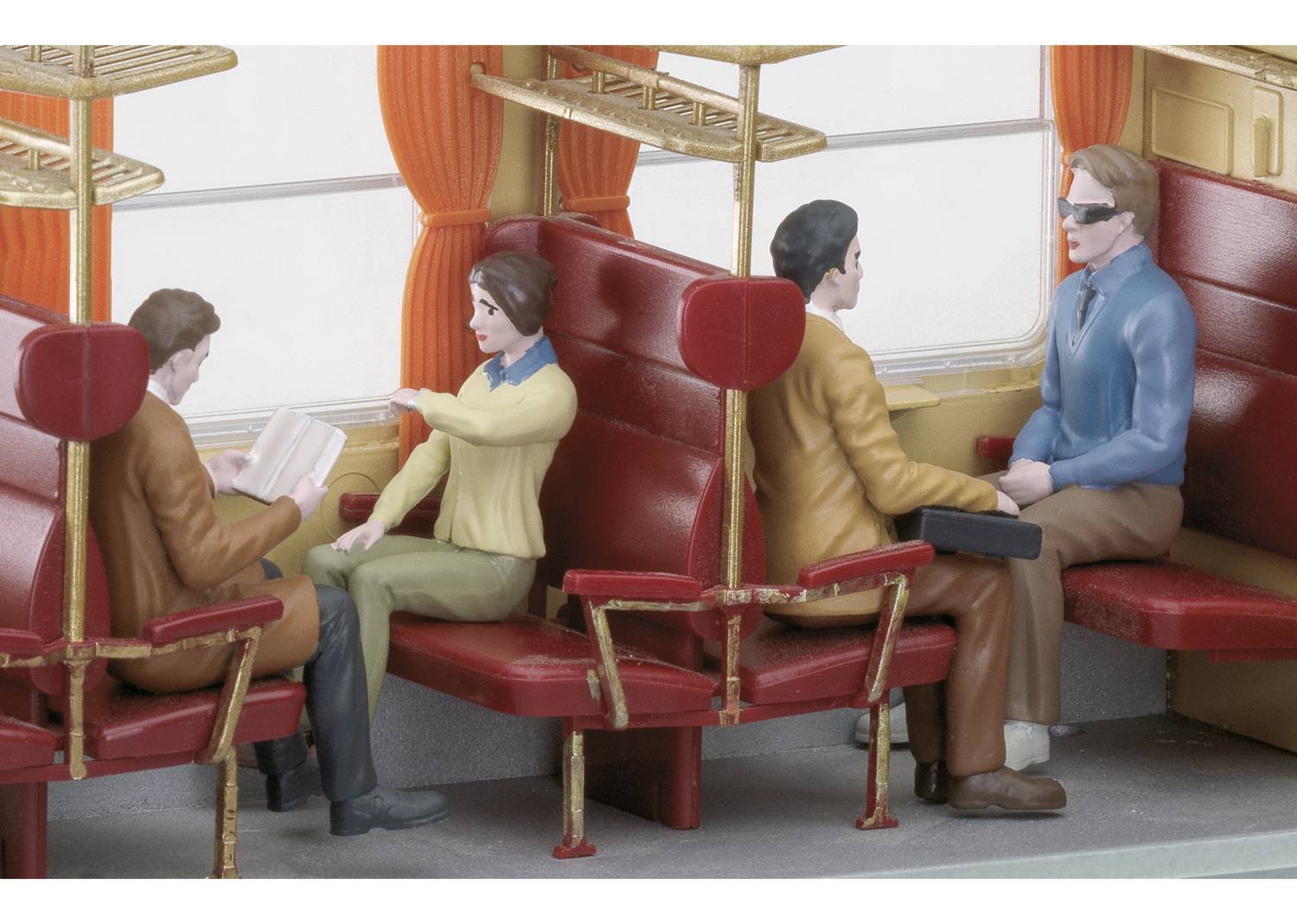 Four figurines in a model train compartment. Two are sitting opposite each other with a book, one is reading aloud with gestures, while two others are listening.