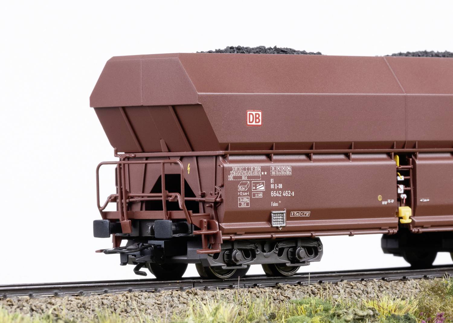 A brown goods wagon of Deutsche Bahn laden with coal stands on a railway track against a white background.
