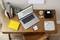 A laptop displays a label design program on a wooden table. Next to it, a label printer, plants, notebook and pen.