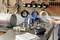 A table with tools, tubes and a label printer. A person is holding a smartphone. Tool wall in the background.