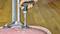 A hand is using a green cordless screwdriver to tighten screws on the underside of an upturned, pink chair.