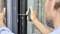 A person is repairing a window frame with a screwdriver, holding a weight-supporting device in the other hand.