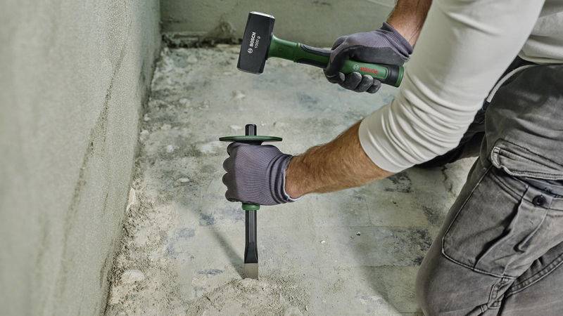 A person is removing old flooring from a concrete floor using a chisel and hammer.