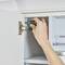 A hand holds a screwdriver and adjusts the hinge of a white kitchen cabinet door.