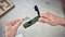 A person is holding a green plastic tool with an open lid in their right hand and a flat silver blade in their left hand. It could be a cutting implement.