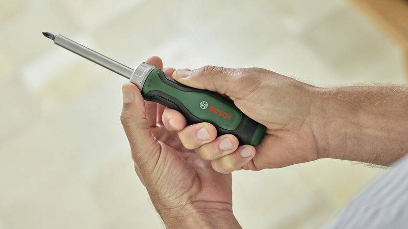 A person is holding a green Bosch screwdriver, ready for use.